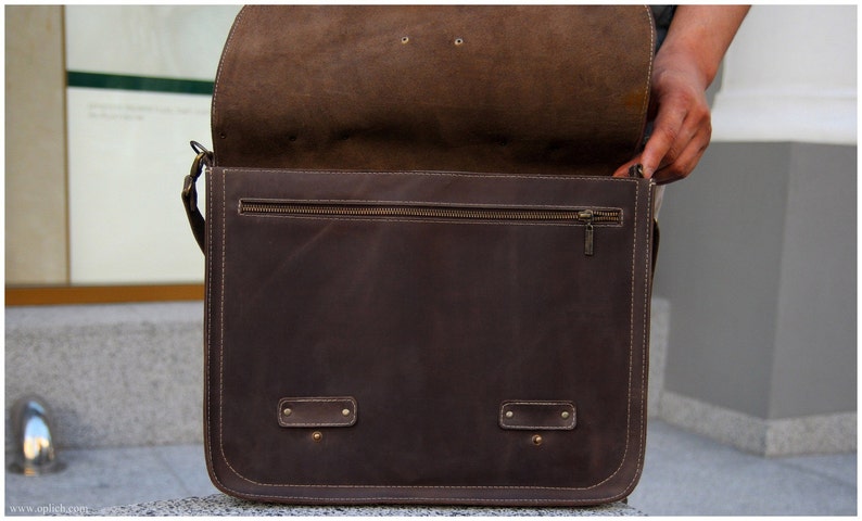 K&ouml;nnte beinhalten: Eine braune Ledertasche mit Rei&szlig;verschlussfach und zwei Schnallen. Die Tasche ist offen und das Innere ist sichtbar.