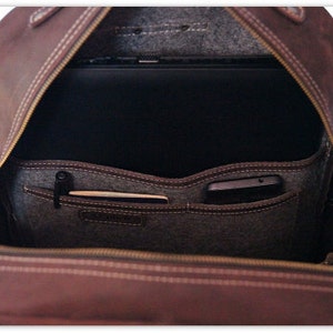 Puede incluir: Mochila de cuero marr&oacute;n abierta con cierre de cremallera. La mochila tiene un forro de fieltro gris y varios bolsillos en el interior. Un port&aacute;til y un tel&eacute;fono son visibles dentro de la mochila.