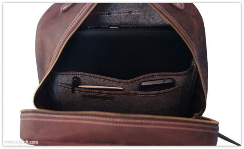 Puede incluir: Mochila de cuero marr&oacute;n abierta con cierre de cremallera. La mochila tiene un forro de fieltro gris y varios bolsillos en el interior. Un port&aacute;til y un tel&eacute;fono son visibles dentro de la mochila.