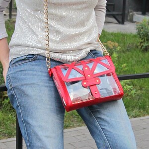 May include: A red and clear plastic crossbody bag with a gold chain strap. The bag has a geometric design and a flap closure with a gold buckle.