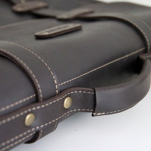 K&ouml;nnte beinhalten: Eine braune Ledertasche mit einem oberen Griff und einem gesteppten Design. Die Tasche hat einen Klappverschluss und eine Messing-Schnalle.