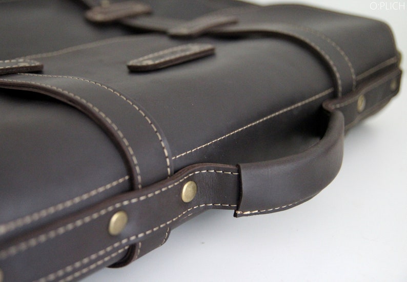 K&ouml;nnte beinhalten: Eine braune Ledertasche mit einem oberen Griff und einem gesteppten Design. Die Tasche hat einen Klappverschluss und eine Messing-Schnalle.