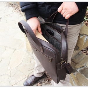 May include: A brown leather briefcase with a zippered closure and a flap. The briefcase has a handle and a shoulder strap. The interior is lined with a gray fabric.