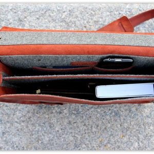 K&ouml;nnte beinhalten: Offene braune Ledertasche mit grauer Filz-Futter. Die Tasche hat mehrere F&auml;cher und ist mit einem Telefon und einem Buch gef&uuml;llt.