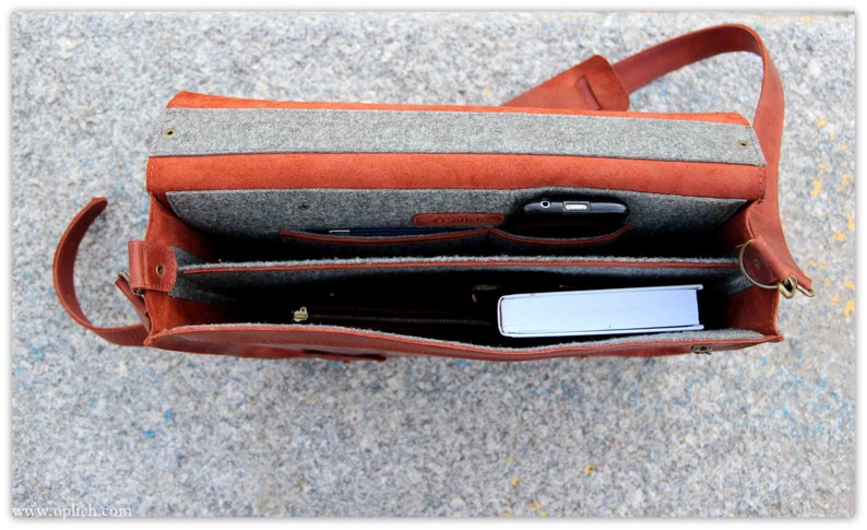 K&ouml;nnte beinhalten: Offene braune Ledertasche mit grauer Filz-Futter. Die Tasche hat mehrere F&auml;cher und ist mit einem Telefon und einem Buch gef&uuml;llt.