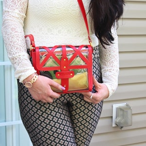 May include: A red and clear crossbody bag with a geometric design. The bag has a gold chain strap and gold accents.