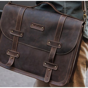 May include: A brown leather messenger bag with a flap closure and adjustable strap. The bag has a stitched design and a metal buckle. The bag has the word "Original" embossed on the front.