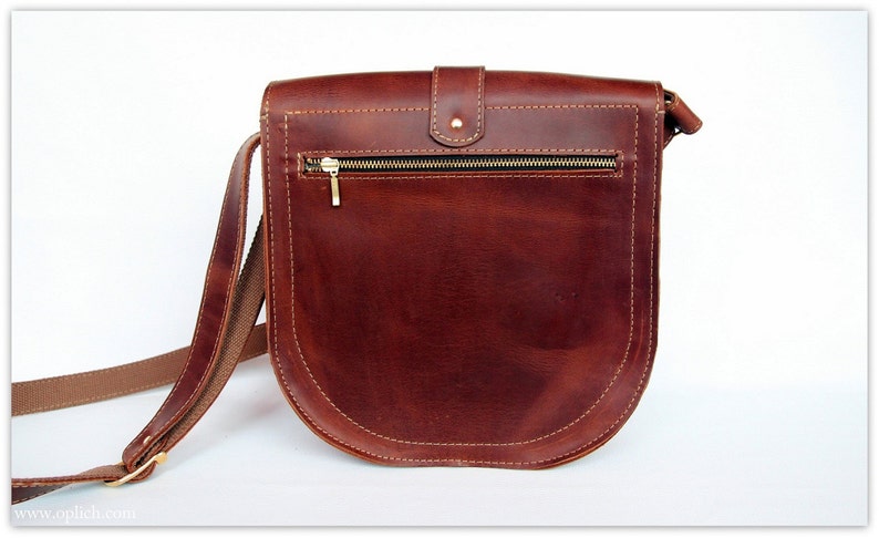 Puede incluir: Bolso bandolera de cuero marr&oacute;n con base curvada y cierre de solapa. El bolso tiene un bolsillo frontal con cremallera dorada y una correa larga y ajustable. Las costuras son de un color m&aacute;s claro.