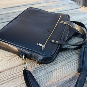 May include: A black leather briefcase with a gold zipper and a long adjustable strap. The briefcase has a textured surface and a flap closure.