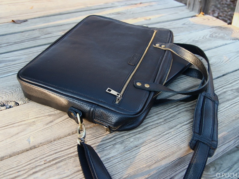 May include: A black leather briefcase with a gold zipper and a long adjustable strap. The briefcase has a textured surface and a flap closure.