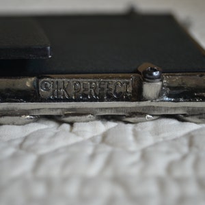 May include: Close-up of a silver picture frame with a black backing. The frame has a braided design and the words "HK PERFECT" are engraved on the bottom.