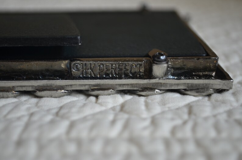 May include: Close-up of a silver picture frame with a black backing. The frame has a braided design and the words "HK PERFECT" are engraved on the bottom.