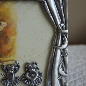 May include: A silver picture frame with a stage curtain design. The frame features two small figurines of ballerinas in silver, and the text "Welcome" is visible at the bottom.