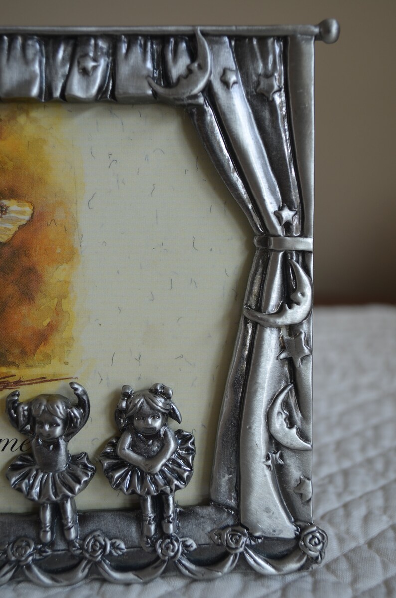 May include: A silver picture frame with a stage curtain design. The frame features two small figurines of ballerinas in silver, and the text "Welcome" is visible at the bottom.