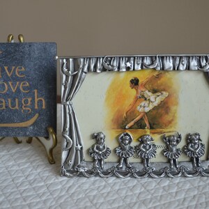 May include: A silver picture frame with a ballerina on stage. The frame has a curtain design and five small ballerinas at the bottom. The frame says "Live Love Laugh" on a slate plaque.