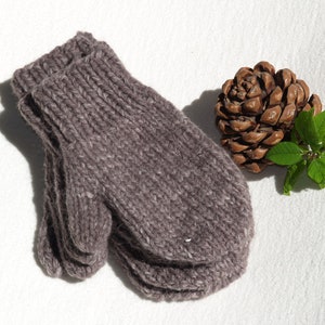 Könnte beinhalten: Ein Paar braune Strickhandschuhe mit gerippter Struktur. Die Handschuhe sind zusammengefaltet und liegen auf einer weißen Oberfläche.