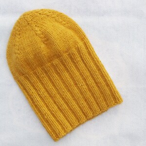Könnte beinhalten: Eine gestrickte Mütze in Senfgelb mit gerippter Struktur.
