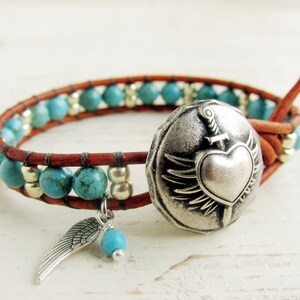 May include: Wrap bracelet with turquoise beads and a brown leather band. Features a silver-tone heart-shaped button with wings and a sword, plus a dangling silver wing charm and turquoise bead. A stylish accessory.