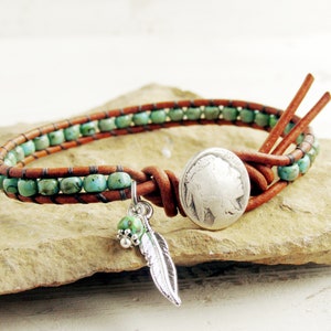 May include: Wrap bracelet with turquoise beads and brown leather. Features a silver-tone feather charm and a large silver button with a Native American profile. The bracelet is approximately 7 inches long.