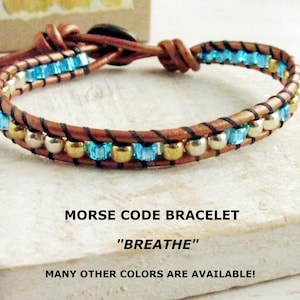 May include: A brown leather wrap bracelet with blue and gold beads. The bracelet is adorned with the text "MORSE CODE BRACELET" and the word "BREATHE". Many other colors are available.
