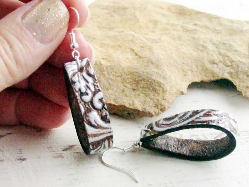 Puede incluir: Un par de pendientes rectangulares con un dise&ntilde;o en relieve marr&oacute;n y blanco. Los pendientes tienen un gancho plateado y un reverso negro. El dise&ntilde;o presenta un patr&oacute;n floral. Los pendientes se muestran sobre un fondo neutro.