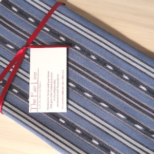 May include: A blue and white striped fabric with a red ribbon tied around it. The fabric has a tag attached to it that says "The Fair Line".