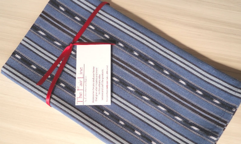 May include: A blue and white striped fabric with a red ribbon tied around it. The fabric has a tag attached to it that says "The Fair Line".