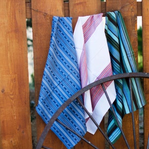 May include: Three striped fabric tea towels hanging on a wooden fence. The towels are blue and white, red and white, and blue and black.