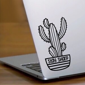 May include: Black and white cactus sticker on a silver laptop with the text "Stay Sharp".