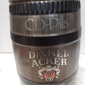 May include: A brown metal keg with a wooden design. The keg is labeled with the text "CD-Pils", "DINKEL ACKER", and "Krömung heimatliches Bmukunst". The keg is 5 liters, 169 US fl. oz., and 1.32 gallons.