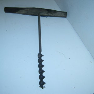 May include: A vintage wooden handled drill bit with a metal auger bit. The bit is black and has a spiral design.