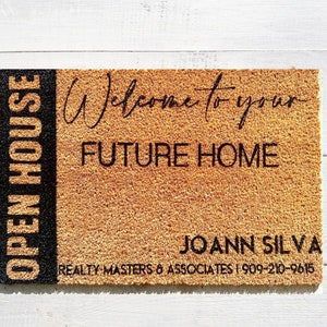 May include: A brown coir doormat with the text "OPEN HOUSE" in black on the left side and "Welcome to your FUTURE HOME" in black on the right side. Below the text is the name "JOANN SILVA" and the text "REALTY MASTERS & ASSOCIATES | 909-210-9615" in black.
