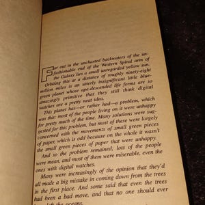 May include: Open book with text on aged paper. The text describes a planet and its inhabitants, discussing their unhappiness and the role of digital watches. The page is slightly yellowed.