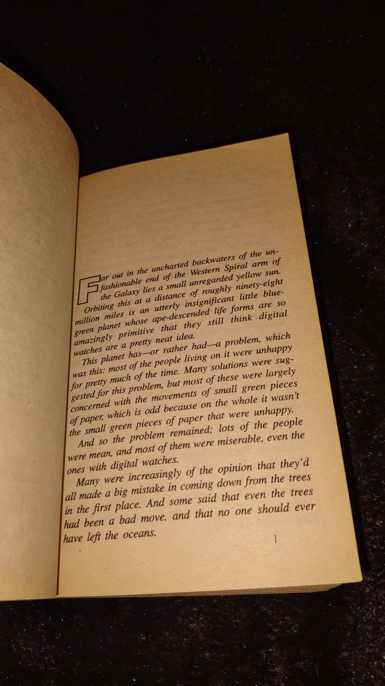 May include: Open book with text on aged paper. The text describes a planet and its inhabitants, discussing their unhappiness and the role of digital watches. The page is slightly yellowed.