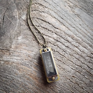 May include: A gold chain necklace with a small harmonica pendant. The harmonica is silver with the words "Suzuki" and "Made in Japan" engraved on it.