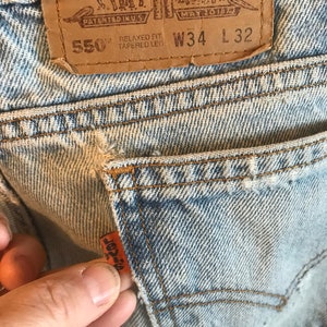 Könnte beinhalten: Hellblaue Jeans aus Denim mit einem braunen Leder-Patch, auf dem "550 Relaxed Fit Tapered Leg W34 L32" steht, und einem kleinen orangefarbenen Levi's-Etikett.