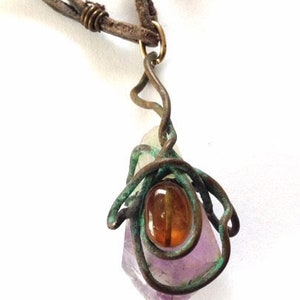May include: A purple and white crystal pendant wrapped in copper wire with a brown leather cord. The crystal is accented with a small amber stone.