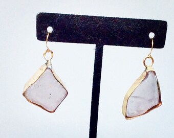 May include: A pair of gold earrings with a white stone. The earrings are on a black stand.