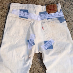 Könnte beinhalten: Weiße Jeans aus Denim mit blauen Denim-Patches und weißem Spitzenbesatz. Die Jeans haben ein Levi's-Etikett auf der Gesäßtasche.