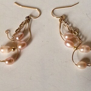 May include: A pair of gold earrings with a delicate chain and multiple pink pearls hanging from each earring.