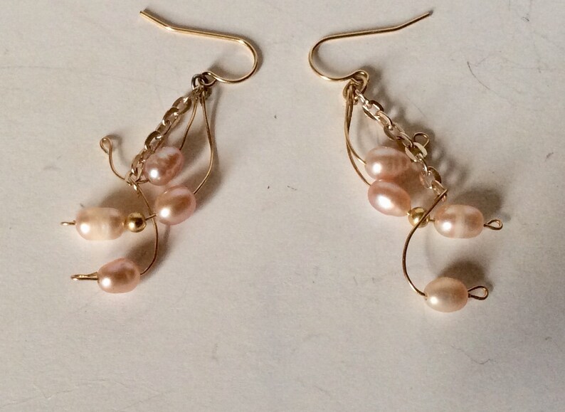 May include: A pair of gold earrings with a delicate chain and multiple pink pearls hanging from each earring.