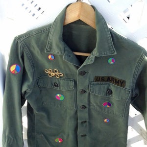 May include: A green military jacket with a US Army patch and several colorful peace sign patches. The jacket has a button-up front and two pockets.