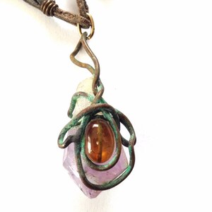May include: A purple amethyst crystal wrapped in copper wire with a brown gemstone pendant. The pendant is attached to a brown leather cord.