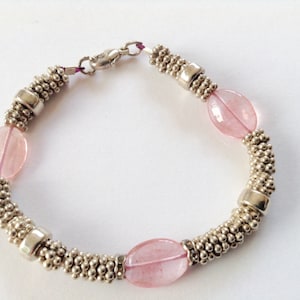 May include: A silver bracelet with pink oval beads. The bracelet has a clasp closure.