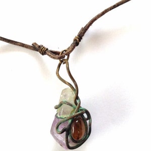 May include: A leather cord necklace with a wire-wrapped pendant featuring a multi-colored crystal and a brown stone.