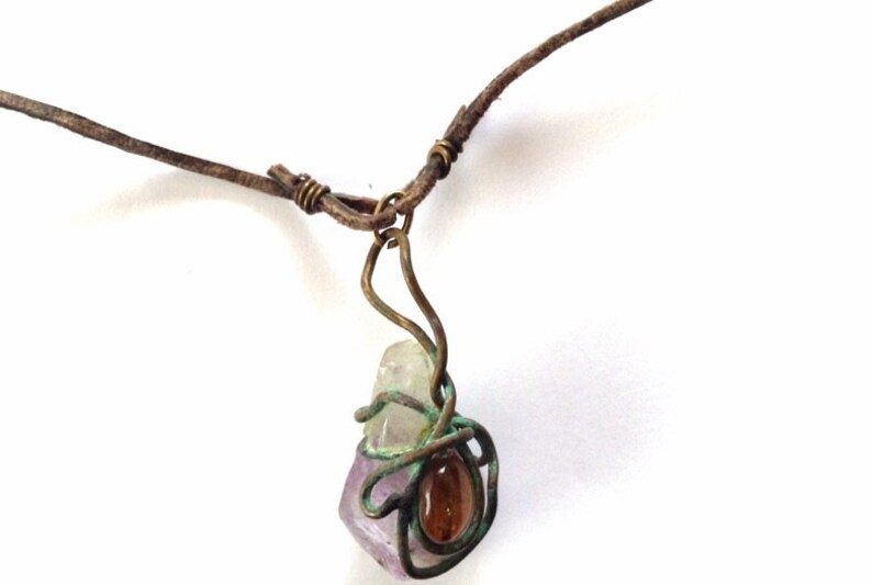 May include: A leather cord necklace with a wire-wrapped pendant featuring a multi-colored crystal and a brown stone.