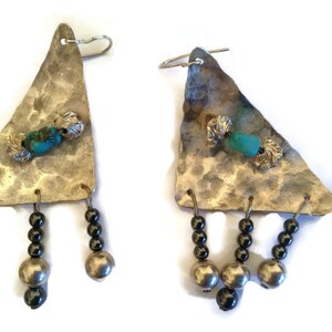 May include: A pair of silver earrings with a triangular shape, featuring turquoise and silver beads. The earrings have a hammered texture and dangle from three black beads.