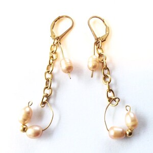 May include: A pair of gold earrings with a chain and pearl accents. The earrings have a hoop design with two pearls on each hoop.