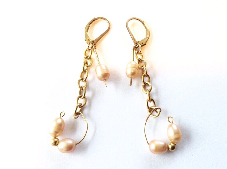 May include: A pair of gold earrings with a chain and pearl accents. The earrings have a hoop design with two pearls on each hoop.