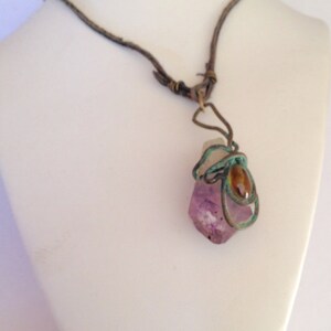 May include: A purple amethyst crystal wrapped in wire with a brown leather cord necklace.